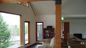 A spacious room with a large window, a wooden staircase, and a bookshelf. - Furano Lodge 10 (Furano)
