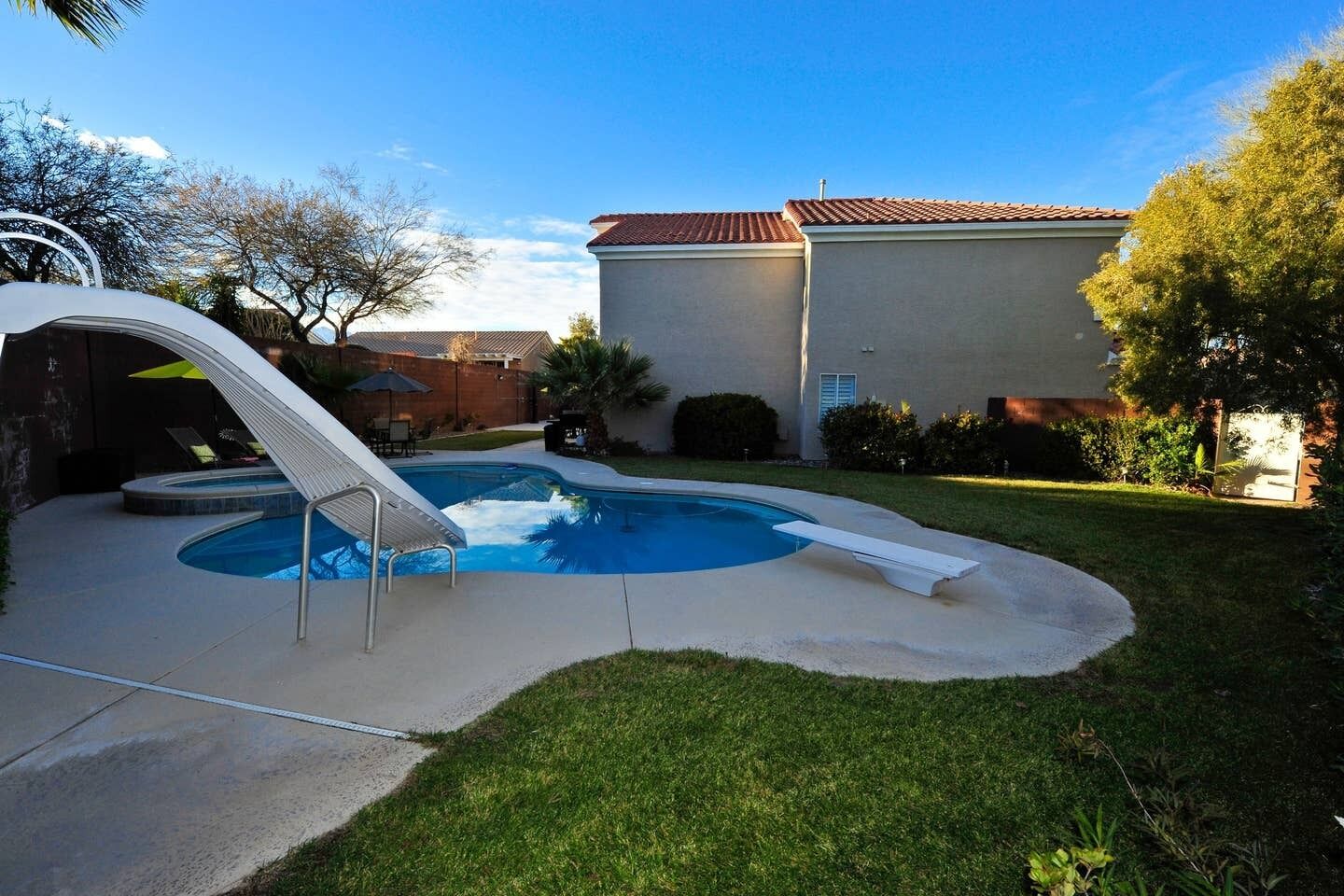A backyard with a swimming pool, a slide, and a house with a tiled roof.