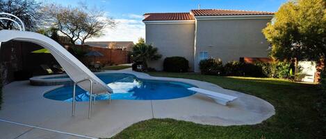 A backyard with a swimming pool, a slide, and a house with a tiled roof.