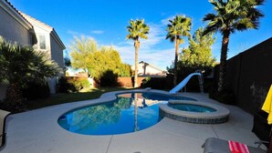 Un jardin avec une piscine, un jacuzzi et un toboggan.