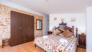 Een slaapkamer met een bed, een kledingkast, een nachtkastje en een klein krukje.