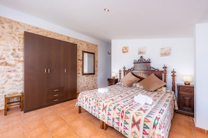 Een slaapkamer met een bed, een kledingkast, een nachtkastje en een klein krukje.