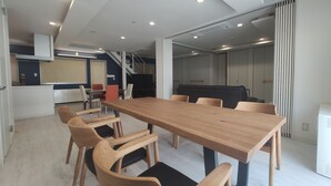 A modern interior with a wooden dining table, beige chairs, a kitchen area, and a staircase leading to another level.