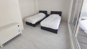 A small, modern bedroom with two single beds, a built-in heater, and a large window.