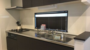 A modern kitchen with a stainless steel countertop, a built-in oven, and a window with blinds. - Villa Paolo (Furano)