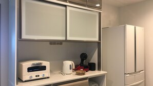 A modern kitchen with a built-in microwave, toaster, and coffee maker on the countertop, a refrigerator, and wooden cabinets. - Villa Paolo (Furano)