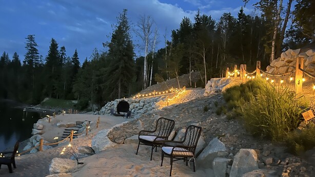 A lakeside seating area with chairs and a stone wall, surrounded by trees and a rocky landscape.