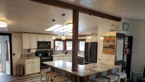 A kitchen with a central island, bar stools, a refrigerator, and a microwave.