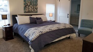 A bedroom with a bed, nightstands, a painting, a door, and a chair.