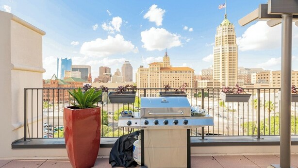 A balcony with a grill, potted plants, and a view of a city skyline.
