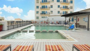 A rooftop pool area with lounge chairs and a building with balconies in the background.