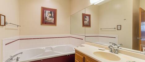 A bathroom with a double sink, a bathtub, and a large mirror.