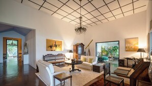 A spacious living room with a large chandelier, a white sofa, a wooden coffee table, and a red rug.
