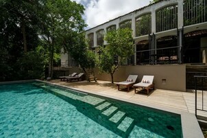 Una piscina con sillas de descanso, rodeada de árboles y un edificio con grandes ventanales.