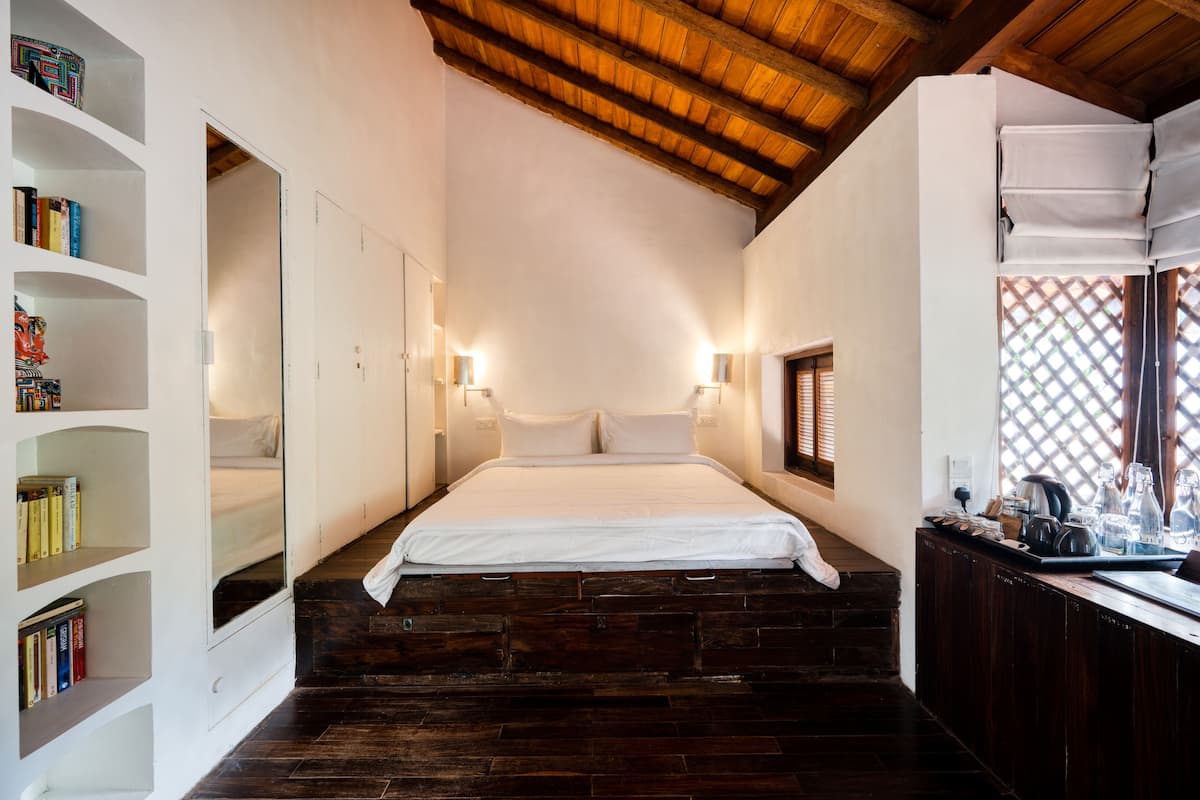Een slaapkamer met een houten plafond, een bed, een boekenkast en een bureau met een raam.
