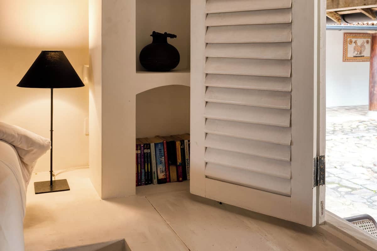Een kamer met een witte deur, een lamp en planken met boeken en decoratieve spullen.