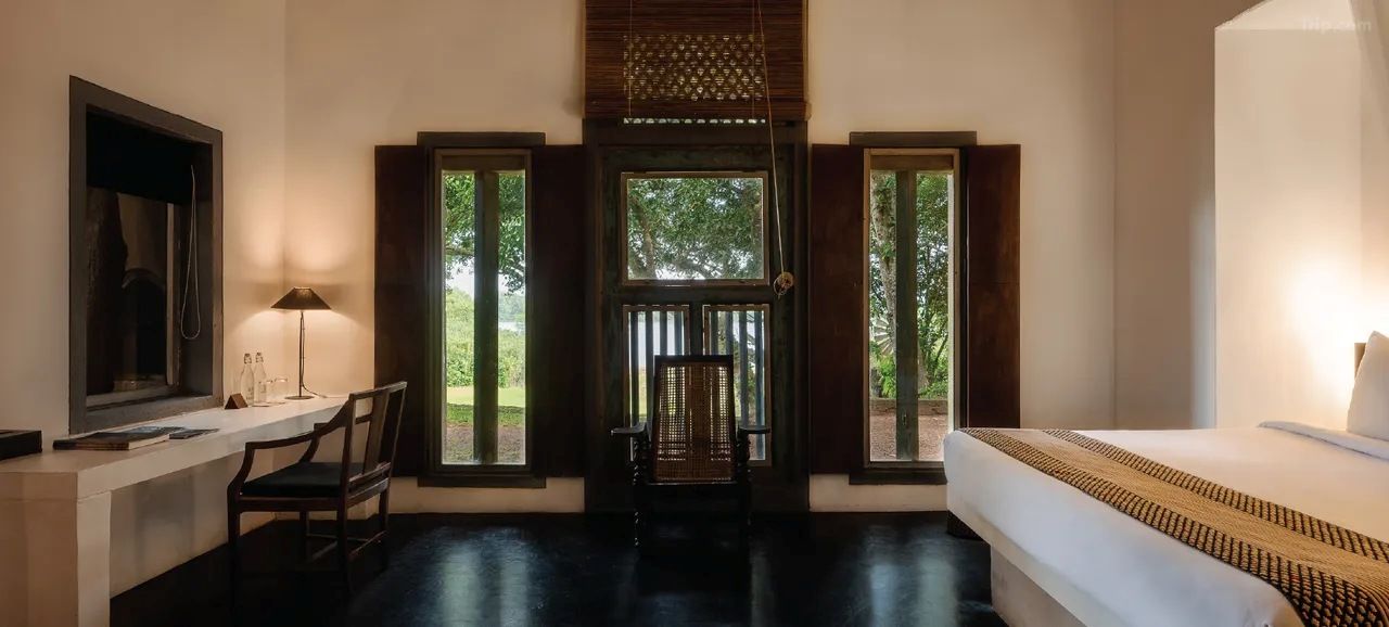 A bedroom with a bed, a desk, a chair, and a window with a view of greenery.
