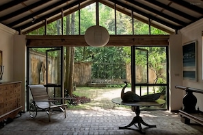A covered outdoor area with a table, chairs, and a swan statue. - Lunuganga Estate (Bentota)