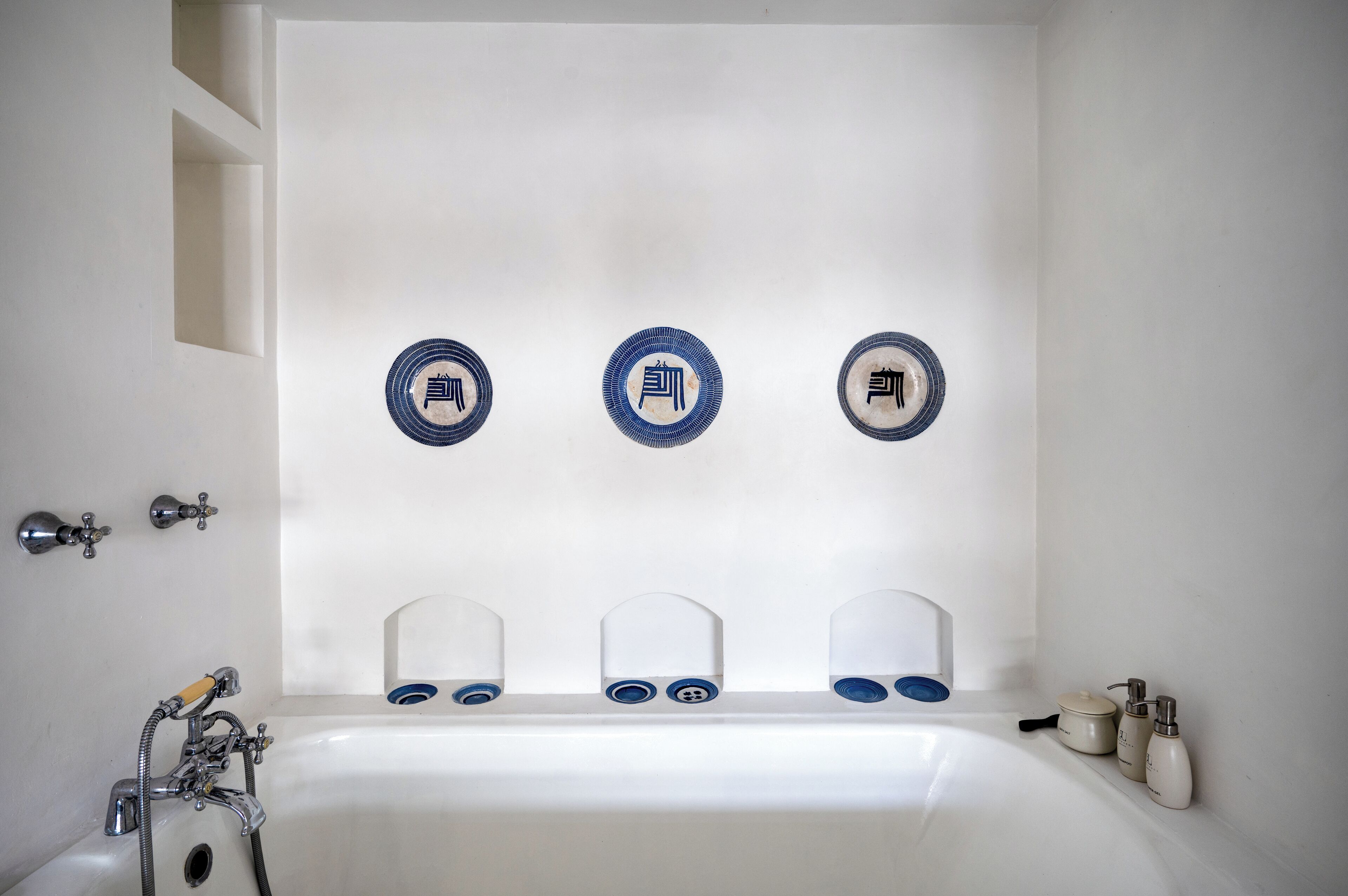 A bathroom with a bathtub, three blue and white decorative plates on the wall, and toiletries on the side.