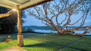 A covered outdoor area with a large tree, a body of water, and a stone pillar.
