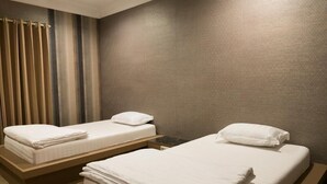 Una habitación de hotel con dos camas individuales, cabecero de madera, una mesita y una cortina.