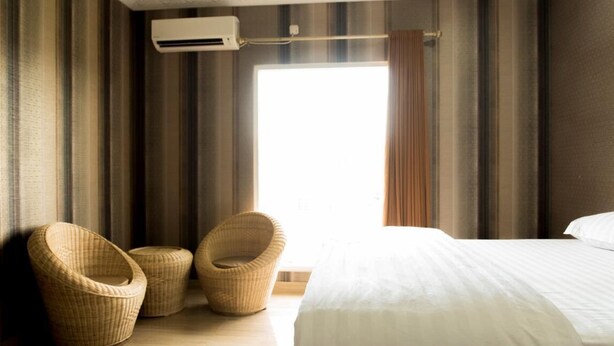 Una habitación de hotel con una cama grande, dos sillones de mimbre, una ventana con cortinas y un equipo de aire acondicionado.