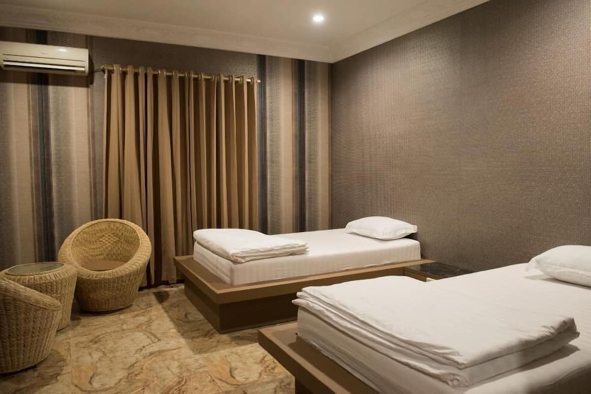 A hotel room with two beds, a small seating area with a chair, and a curtain.