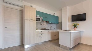 Una cocina moderna con alacenas de madera clara, microondas integrado y un televisor de pantalla plana montado en la pared.
