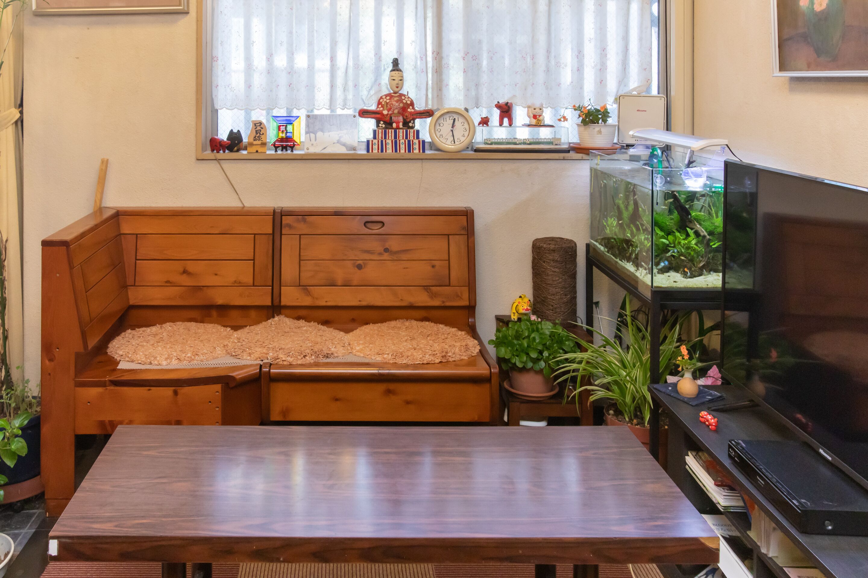 Una sala de estar con un sofá de madera, un televisor, un acuario y diversos objetos decorativos en el alféizar de la ventana.