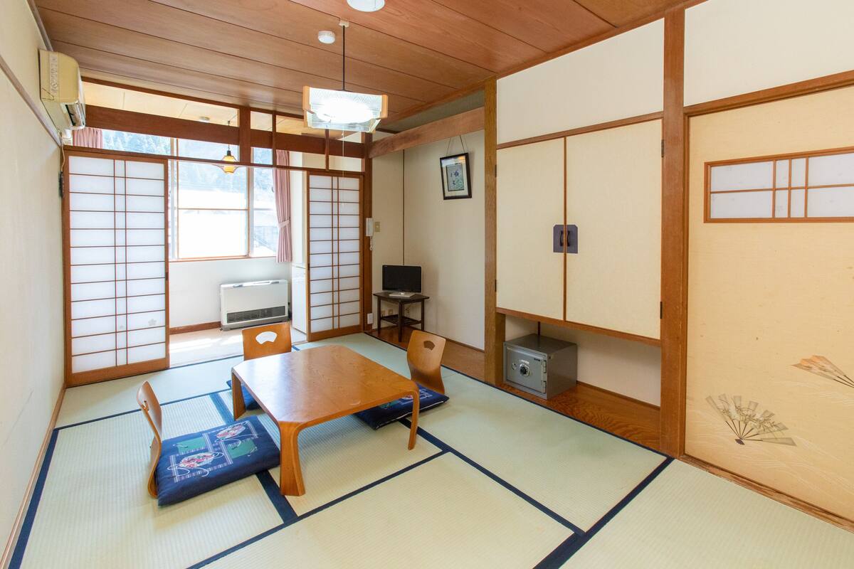 Et traditionelt japansk rum med tatamimåtter, et træbord, et fjernsyn og et lille skab.