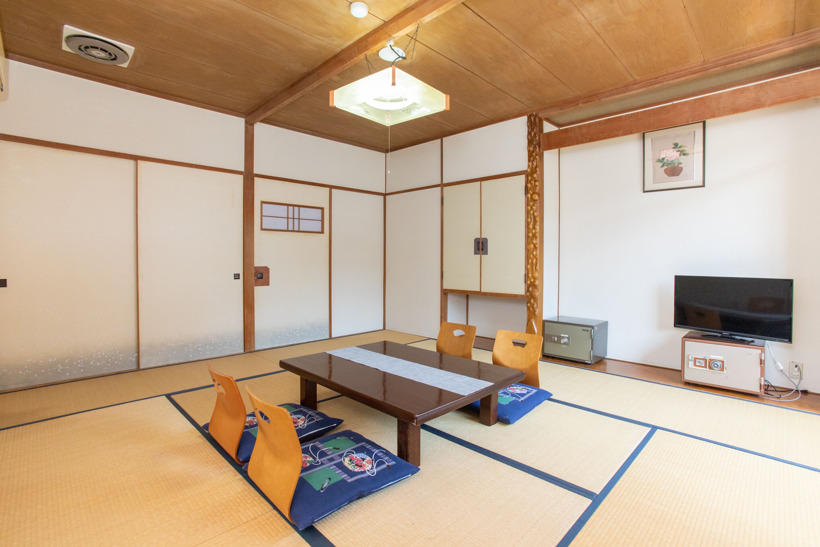 Et traditionelt japansk rum med tatamimåtter, et lavt bord, træstole og et fjernsyn.