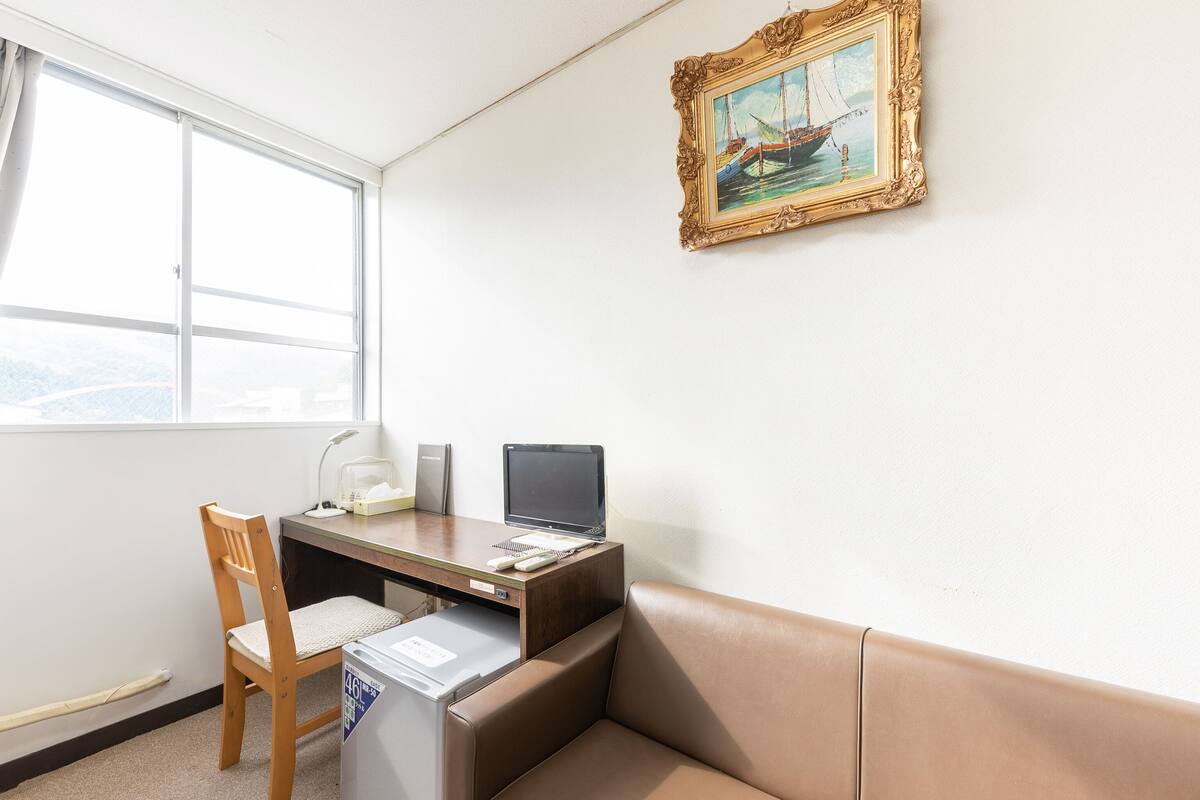 Et værelse med skrivebord, stol og et lille køleskab.