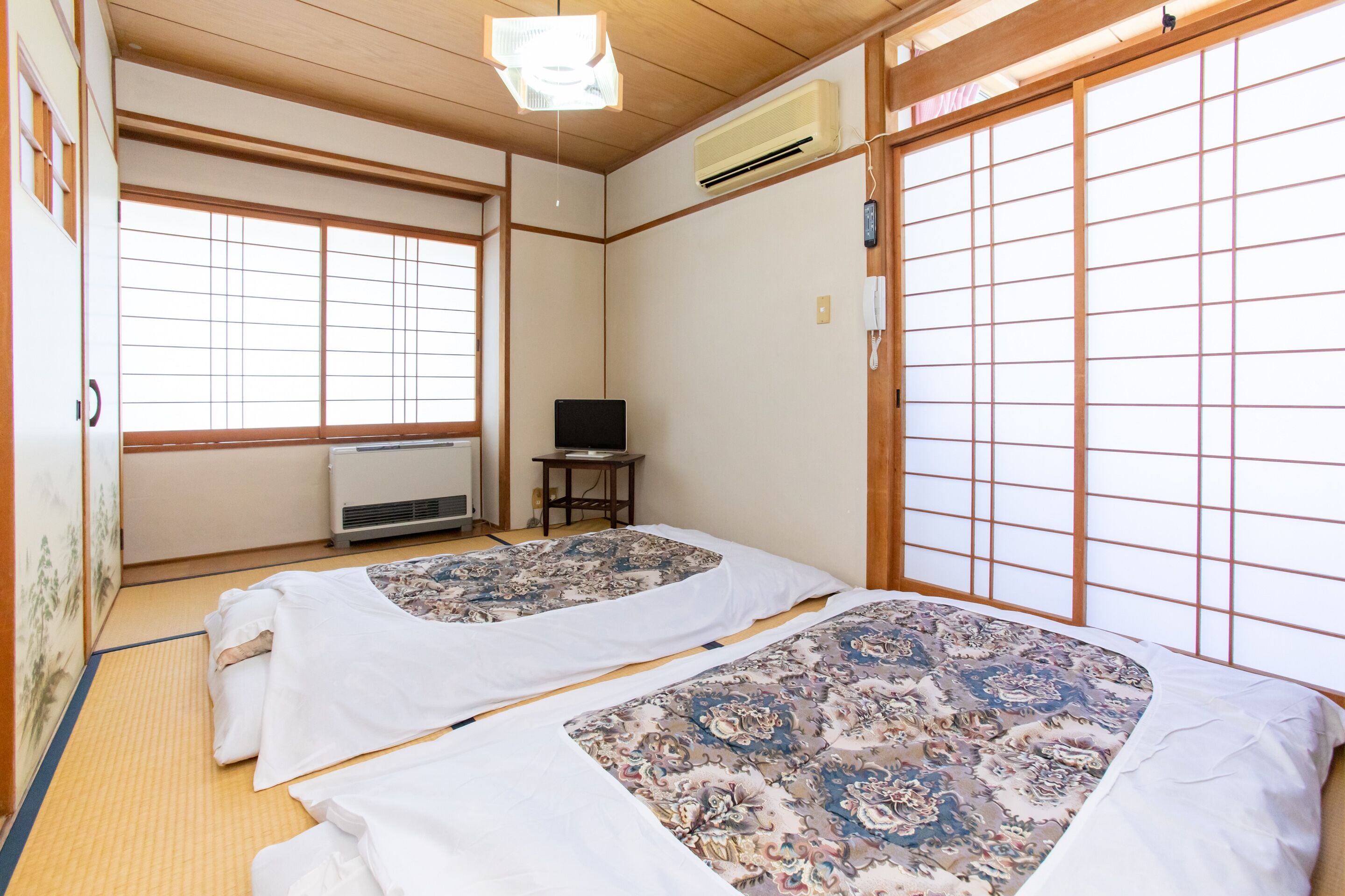 Perinteinen japanilainen huone, jossa on tatamimatto, kaksi tatamipatjaa kukka-aiheisilla vuodevaatteilla, televisio ja liukuovi.