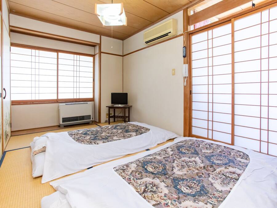 Perinteinen japanilainen huone, jossa on tatamimatto, kaksi tatamipatjaa kukka-aiheisilla vuodevaatteilla, televisio ja liukuovi.