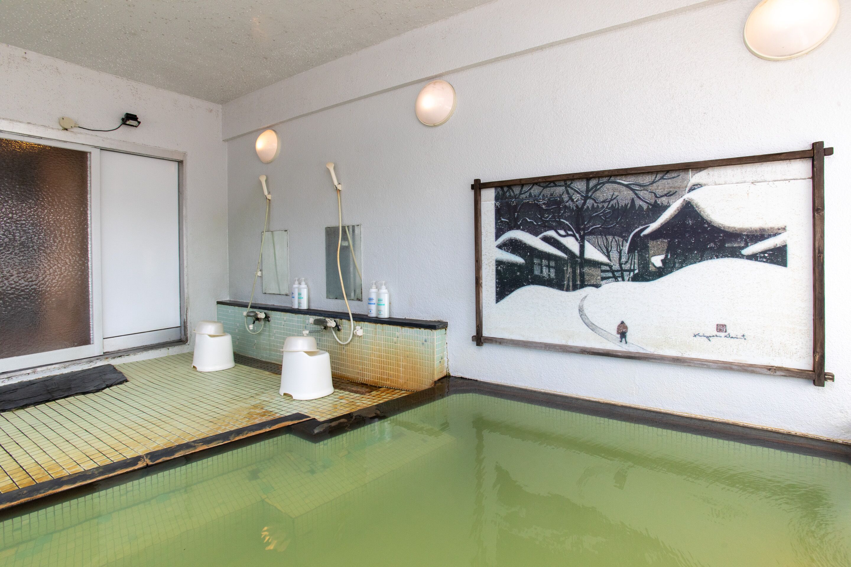 A spa area with a green-tiled floor, a large painting of a snowy landscape, and a mirror above the sink.