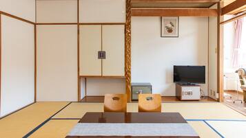 A tatami mat room with a low table, two wooden chairs, a television, and a small safe.