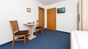 A room with a bed, a desk, two chairs, a small table, and a television on the wall. - Single room in the Hotel-Pension Marlies - Single room (Neuharlingersiel)