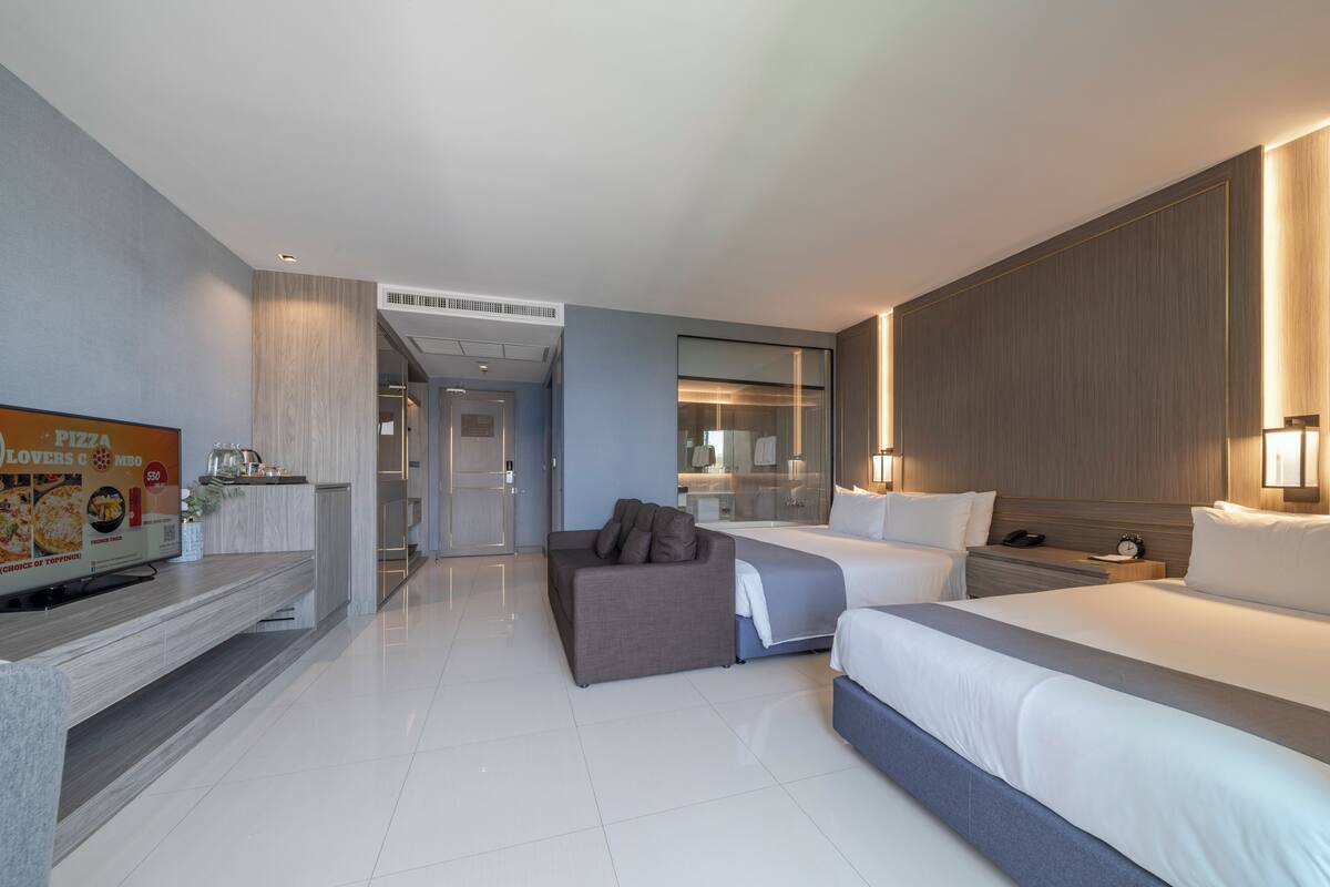 Habitación de hotel con cama, sofá, televisión, minibar y baño a la vista.
