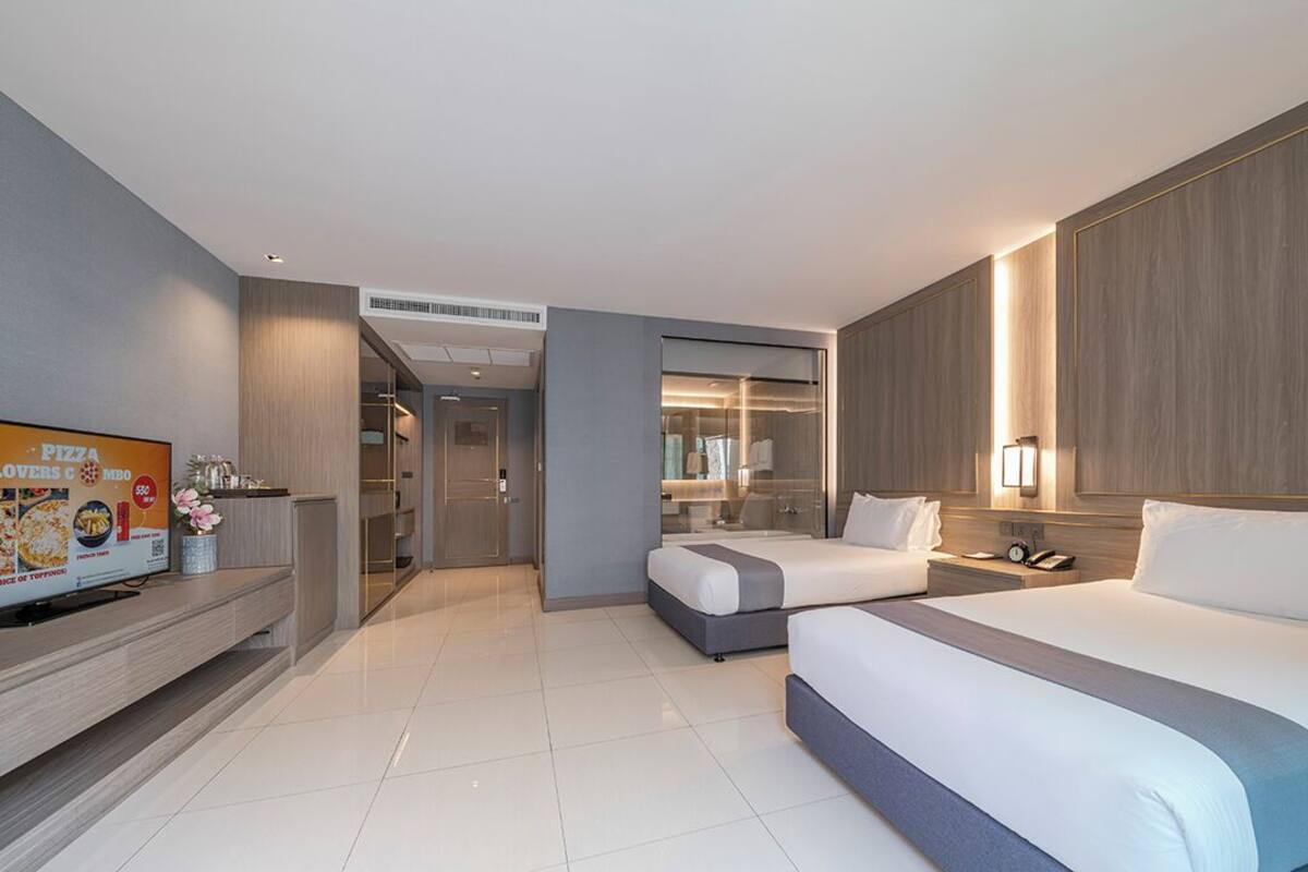Una habitación de hotel moderna con dos camas, un televisor y un baño visible a través de una puerta de vidrio.