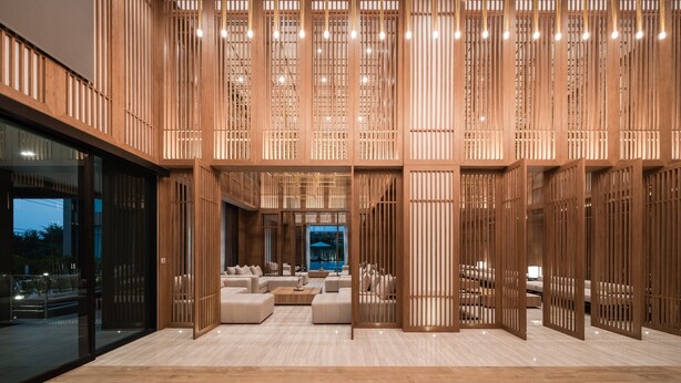 Un interior moderno con zona de estar, separadores de madera y vista a una piscina.
