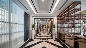 Un moderno vestíbulo de hotel con un piso de mármol geométrico, ventanas amplias y una estantería de metal decorativa.