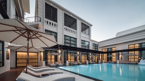 Una piscina interior con sillas de descanso y sombrillas, rodeada por un edificio moderno con grandes ventanales y balcones.