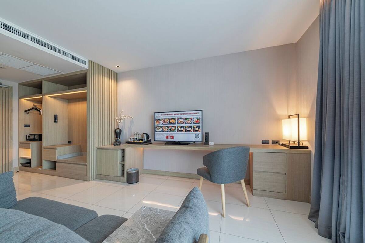 Una habitación de hotel moderna con televisión de pantalla plana, un escritorio, una silla y un sofá.