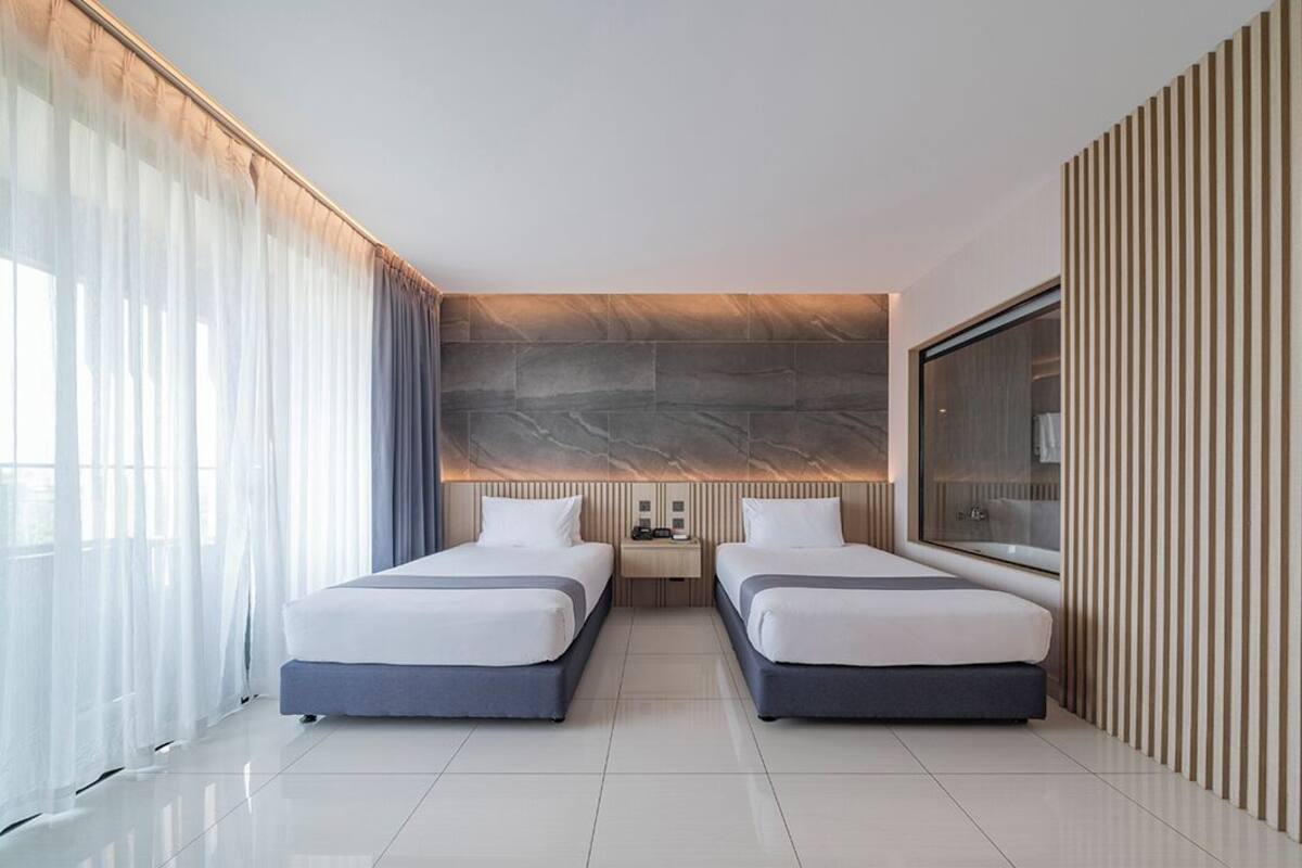 Una habitación de hotel moderna con dos camas, un espejo grande y una pared decorada con piedra.