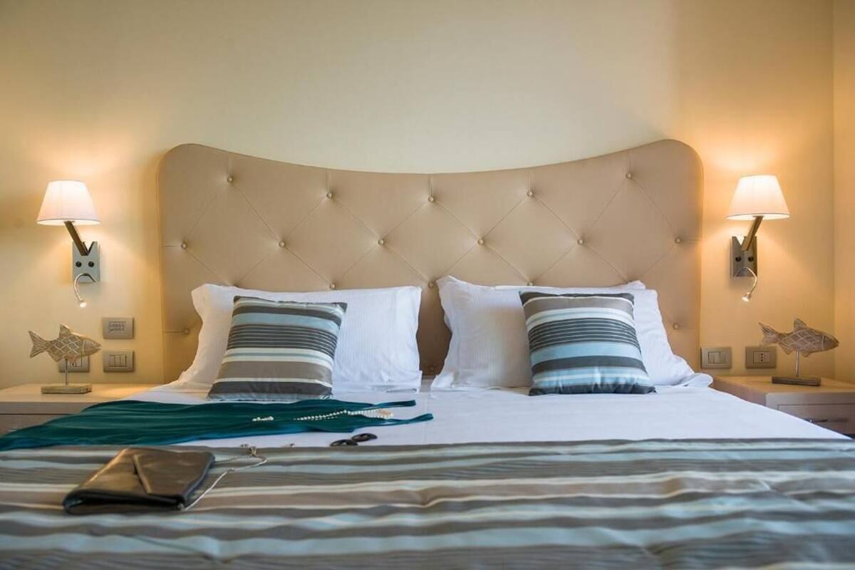 Een net opgemaakt bed met gestreept beddengoed, twee kussens en een opgevouwen portemonnee op het bed.