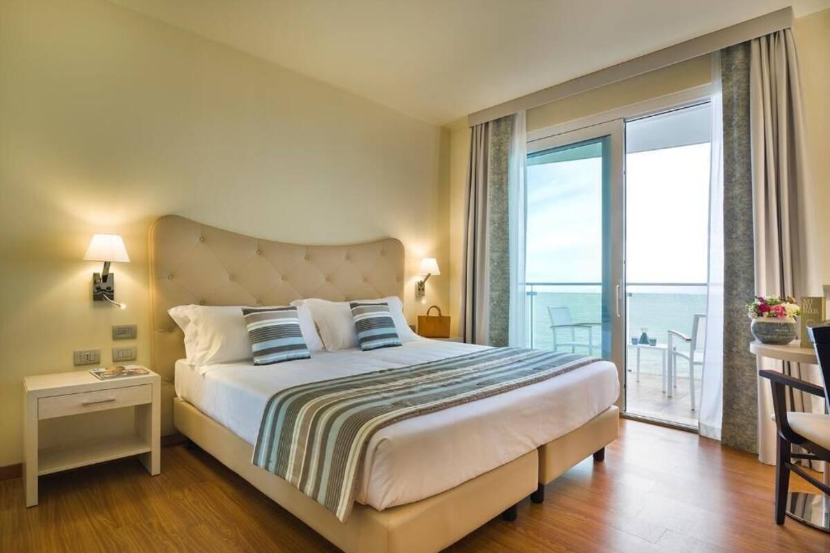 Een hotelkamer met een groot bed, een nachtkastje, een stoel en een balkon met uitzicht.