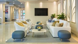Eine moderne Hotelhalle mit weißen Sofas, einem Flachbildfernseher und einem großen Fenster.