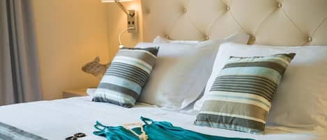 A neatly made bed with striped pillows, a teal garment, and a lamp on the nightstand.