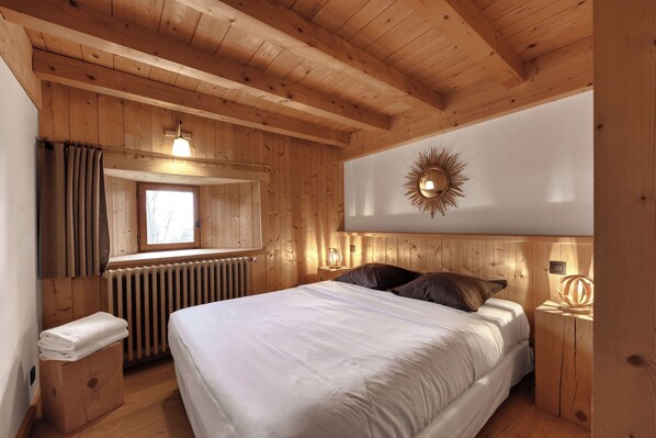 Un dormitorio con paneles de madera, una cama, un ventanal, un radiador y una lámpara fijada a la pared.
