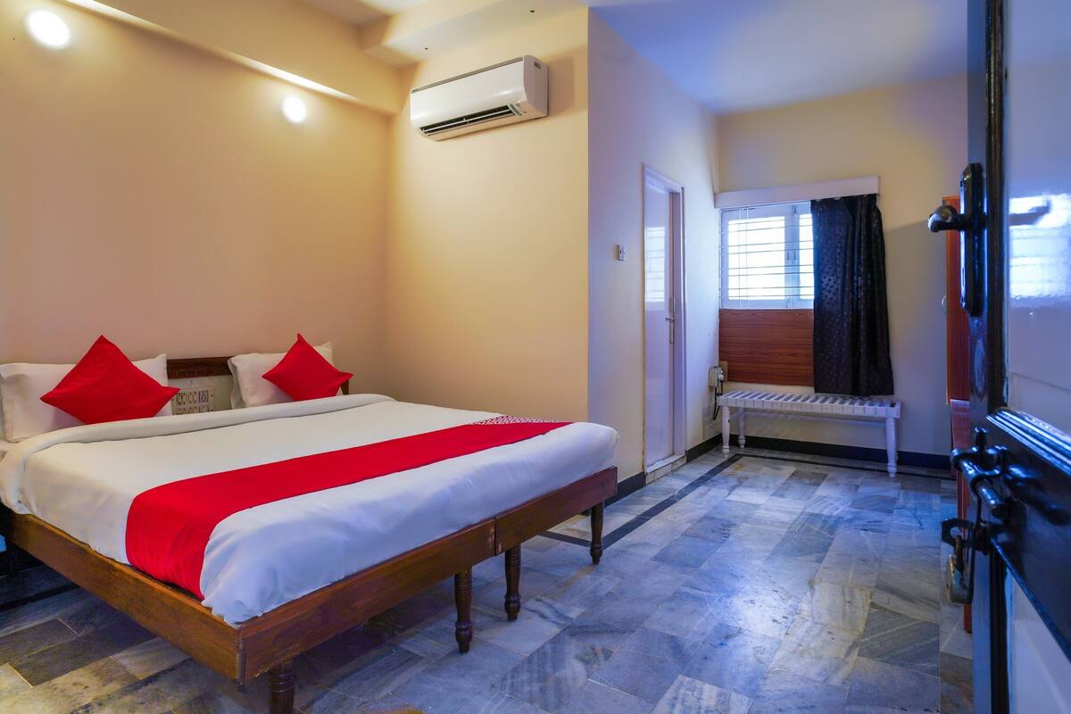 Quarto de hotel com cama, um banco, ar condicionado e uma porta.